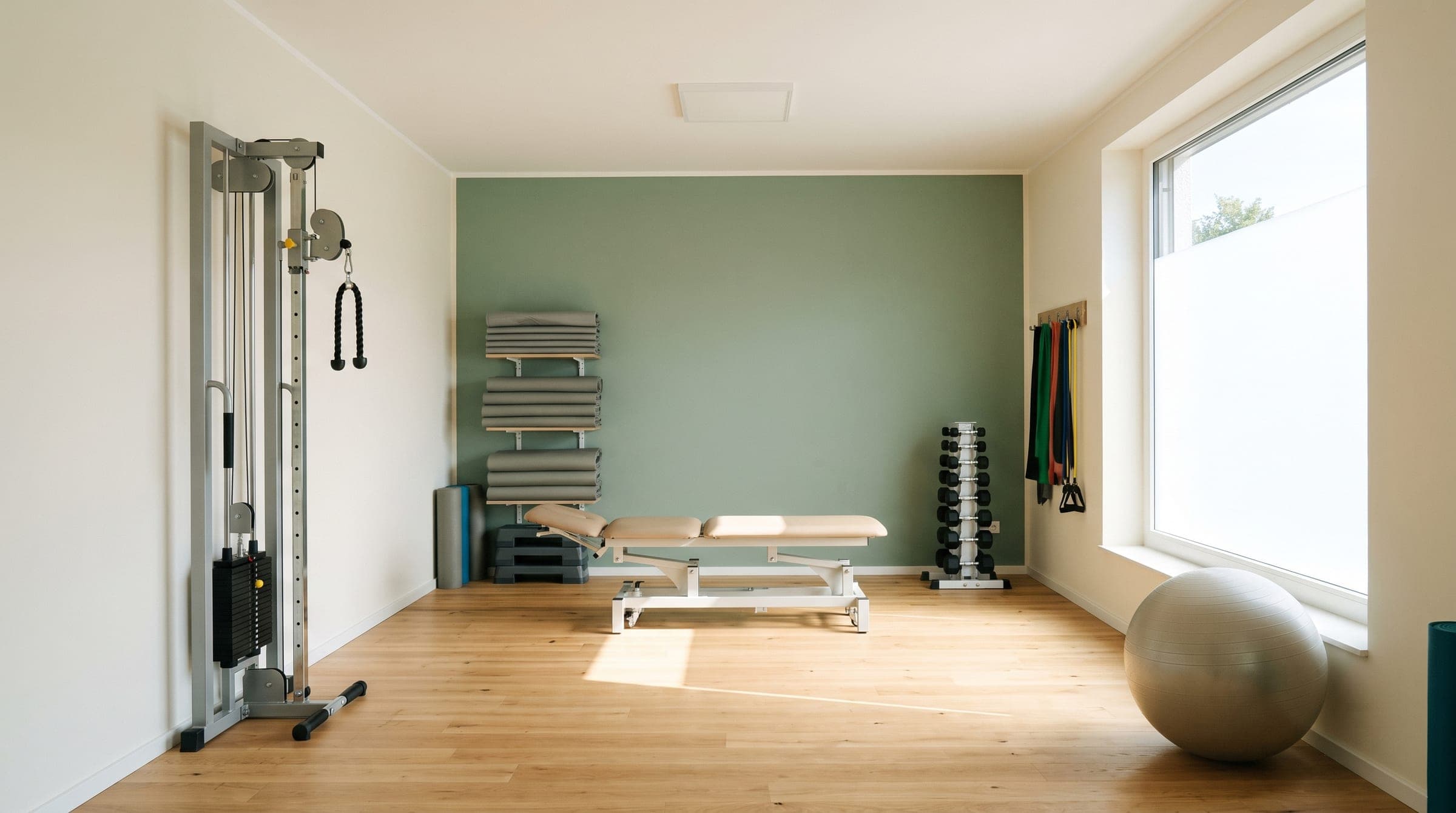 Trainingsbereich einer Physiotherapiepraxis mit Zugapparat, Therapieliege, Matten und Hanteln